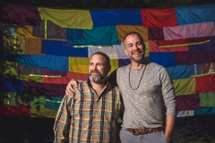 Two men pose for a photo in front of a Site Lines collection of colored fabric during the gala at the Karl Stirner Arts Trail.