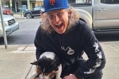 A man wearing a Mets baseball cap gives a big smile while holding a dog.