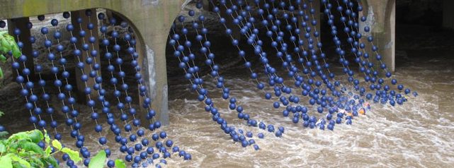 The outdoor installation Bushkill Curtain by Stacy Levy on the Karl Stirner Arts Trail in Easton, Pennsylvania, features strands of blue balls on strings that hang from a bridge and reach down into the Bushkill Creek.