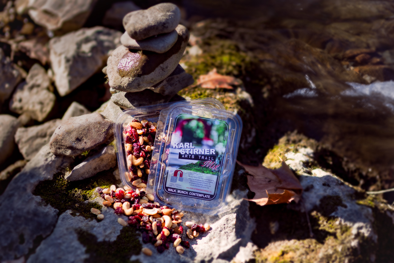 An open box and a closed box of trail mix with the branding of the Karl Stirner Arts Trail are on some rocks