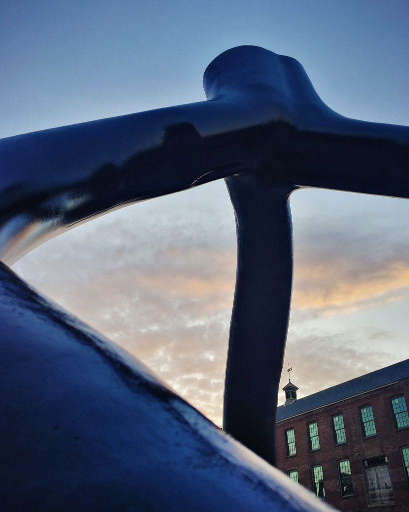 A portion of a winding metallic sculpture by Stephen Tobin with a brick building in the background on the Karl Stirner Arts Trail in Easton, Pennsylvania