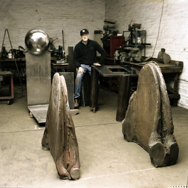 Artist Karl Stirner sits in a studio with machinery and his sculpture Hounds of Hell, comprised of two large pieces of iron that look like book ends, which is now displayed on the Karl Stirner Arts Trail in Easton, Pennsylvania.