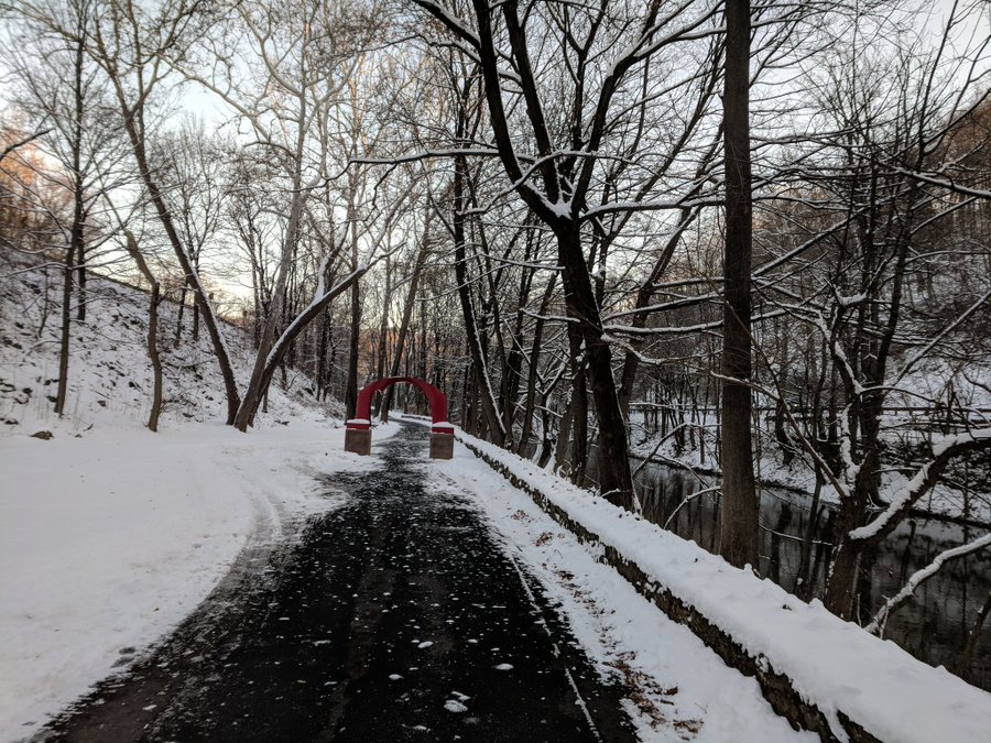 Snow covers the ground and trees by the walking trail and iconic red arch sculpture on the Karl Stirner Arts Trail in Easton, Pennsylvania.