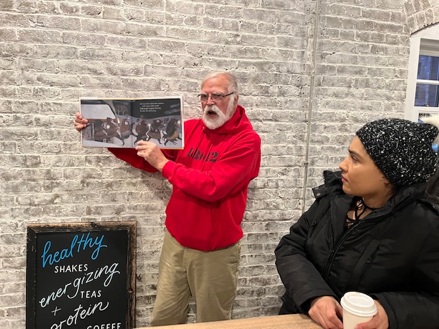 A man holds open a book to show the pictures as he tells the story while someone watches People gather inside Thrive Easton at Silk during the Fifth Annual Winter Solstice Walk at the Karl Stirner Arts Trail in Easton, Pennsylvania.