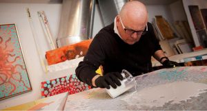 Ed Kerns pours a white liquid from a glass container as part of the process to create an artwork.