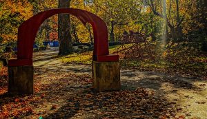 The iconic red arch sculpture amid autumn leaves and the Late Bronze Root sculpture behind it on the Karl Stirner Arts Trail in Easton, Pennsylvania.