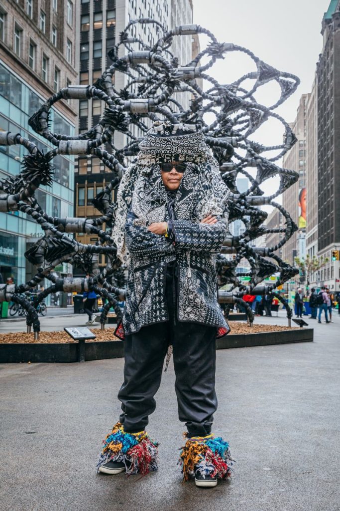 Sculptor Chakaia Booker wears a headdress she made for herself and stands in front of her 35-foot-tall Shaved Portions, a sculpture made of discarded tires on the pedestrian plaza on Broadway in New York City’s Garment District between 39th and 40th streets.