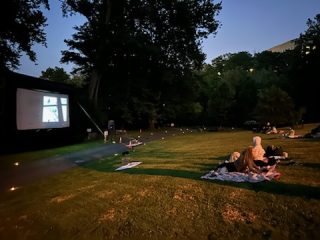 People sit in chairs and on the grass as they watch the film At Eternity's Gate on a big outdoor screen during the Movies Along the Trail event on the Karl Stirner Arts Trail in Easton, Pennsylvania.