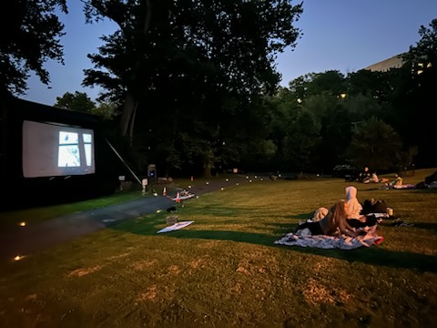 People sit in chairs and on the grass as they watch the film At Eternity's Gate on a big outdoor screen during the Movies Along the Trail event on the Karl Stirner Arts Trail in Easton, Pennsylvania.