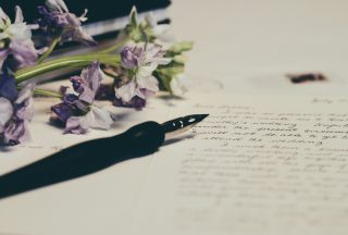 Poetry written in cursive on paper with a pen and purple flowers also on the paper