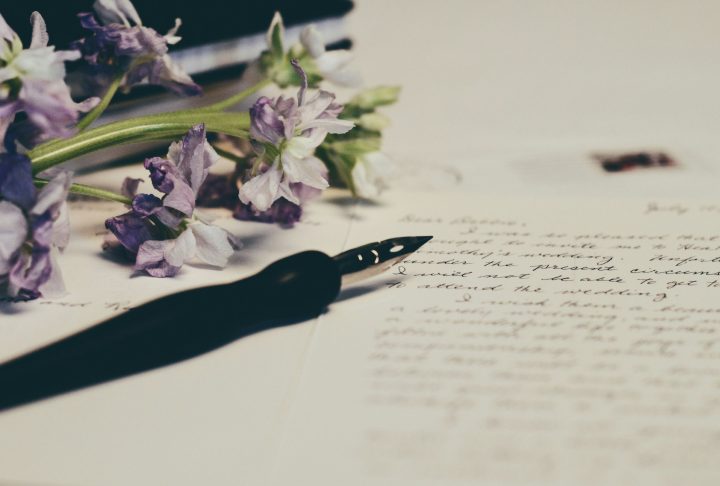 Poetry written in cursive on paper with a pen and purple flowers also on the paper