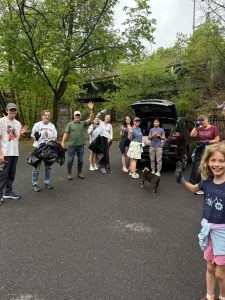 Ten local residents and Lafayette College students, many of them waving and some carrying black garbage bags, pose for a photo during a cleanup event on the Karl Stirner Arts Trail in Easton, Pennsylvania.