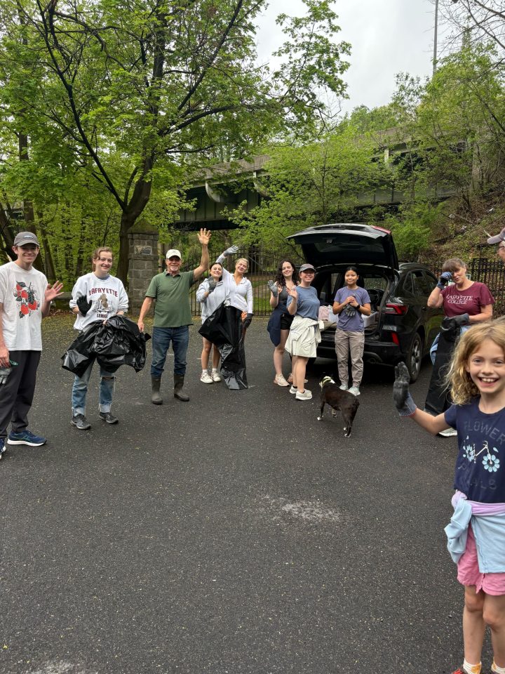Ten local residents and Lafayette College students, many of them waving and some carrying black garbage bags, pose for a photo during a cleanup event on the Karl Stirner Arts Trail in Easton, Pennsylvania.