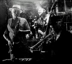 A black and white photo of a saxophone player, bass player, and trumpet player in concert