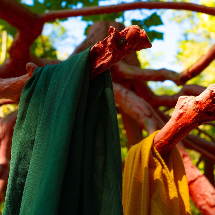 A piece of green fabric and a piece of yellow fabric rest on the red Late Bronze Root sculpture by Steve Tobin on the Karl Stirner Arts Trail in Easton, Pennsylvania.