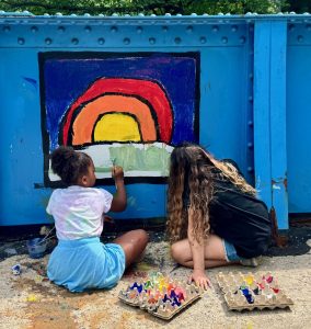 Two girls paint the sun against a blue sky on the Young Masters Wall on the Karl Stirner Arts Trail in Easton, Pennsylvania.