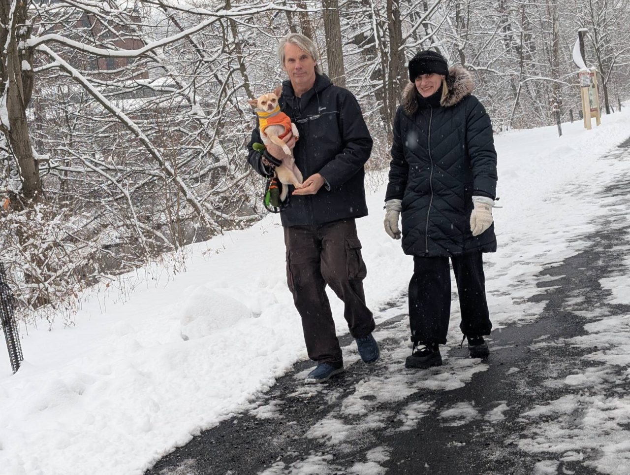 A man holds a dog while walking next to a woman on a snowy day along the Karl Stirner Arts Trail in Easton, Pennsylvania.