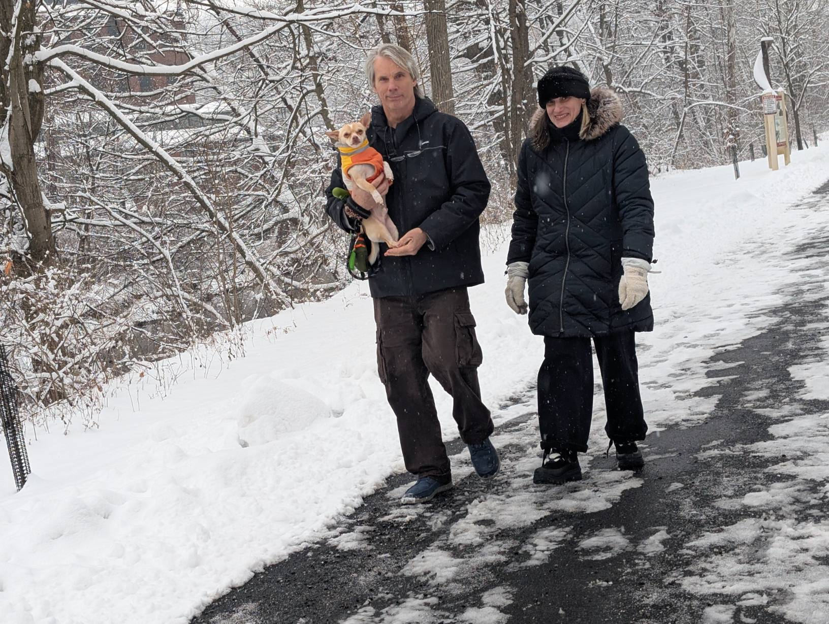 A man holds a small dog while walking next to a woman on a snowy day on the Karl Stirner Arts Trail in Easton, Pennsylvania.